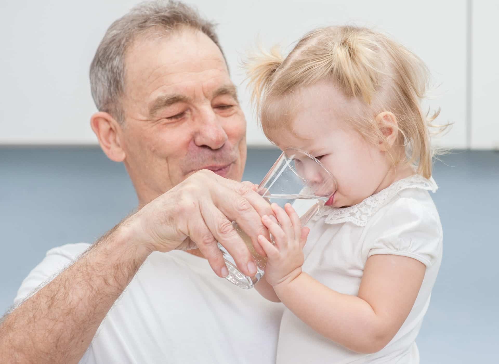 Kind und ältere Person trinken Wasser am Tisch als Symbol für Wasserqualität, Gesundheit, Flüssigkeitszufuhr und besondere Sensibilität in verschiedenen Lebensphasen.